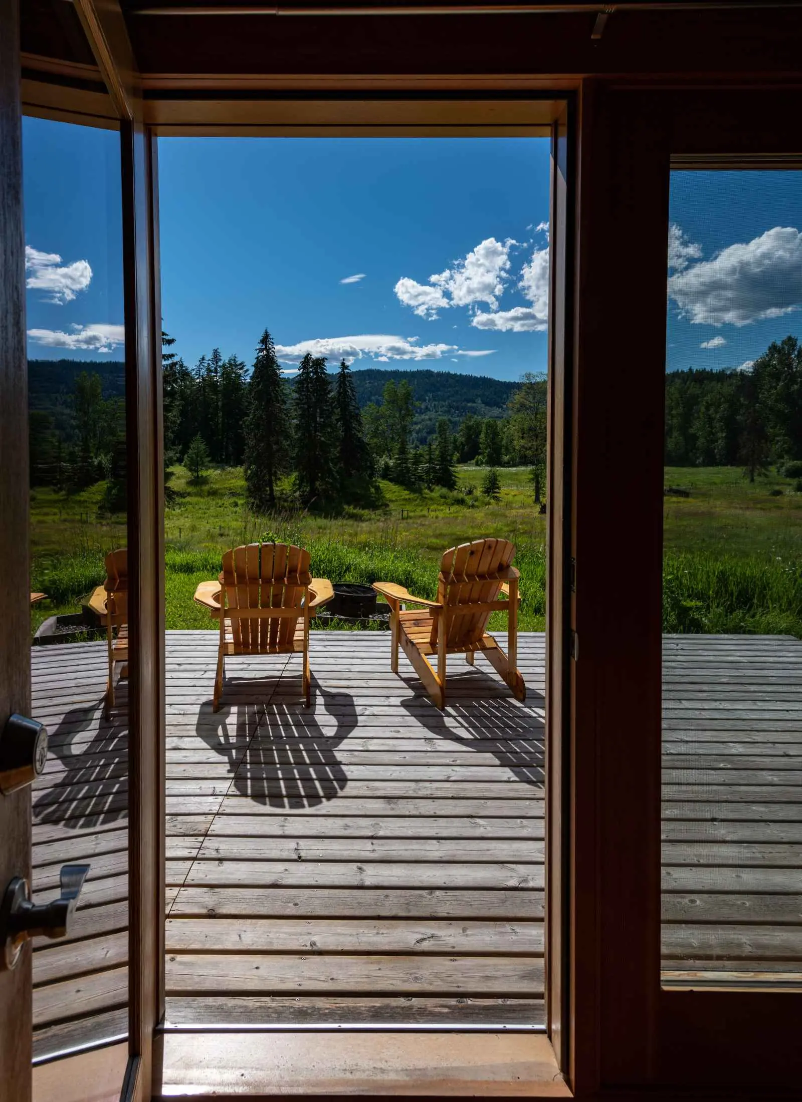 Wooden chairs on a sunlit cabin deck at Kayanara, framed by the open doorway.