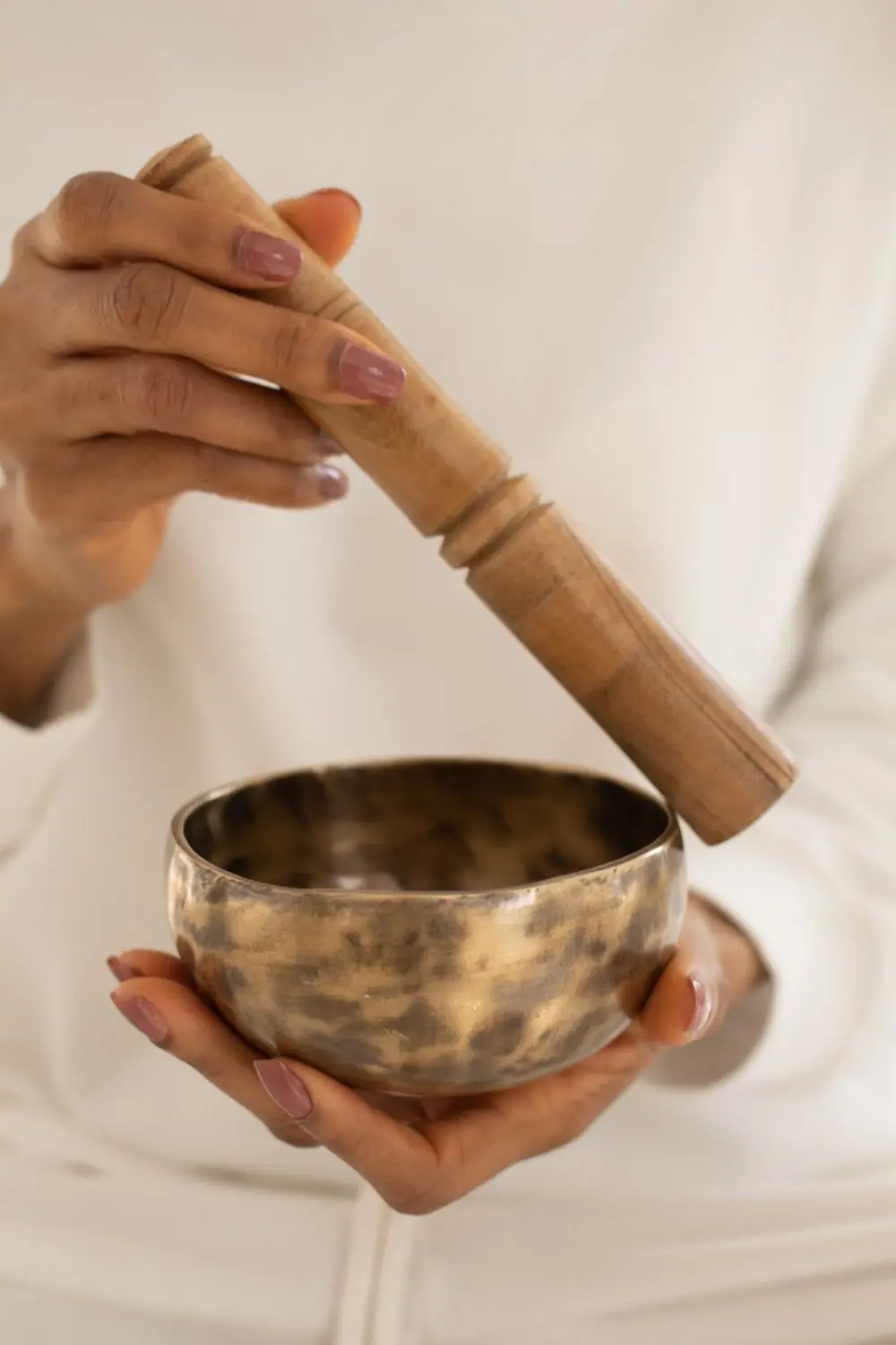 A close view of hands holding a bronze singing bowl and a wooden striker.